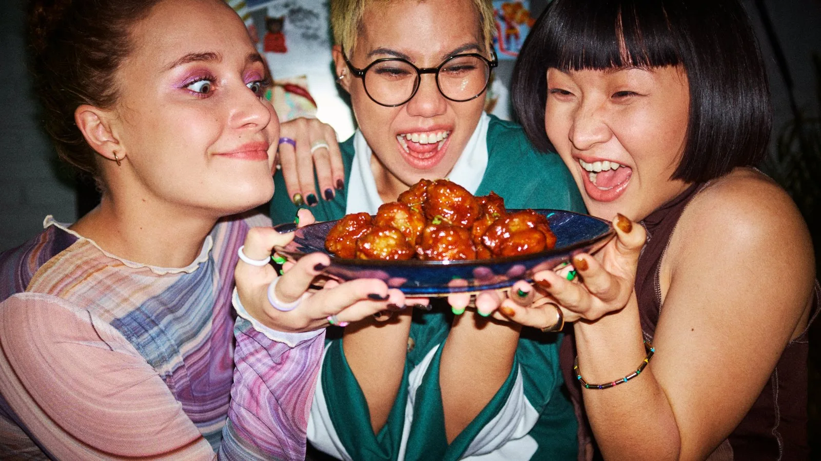 A still from the bibigo campaign — three people laughing as they hold out a plate of Korean fried chicken.